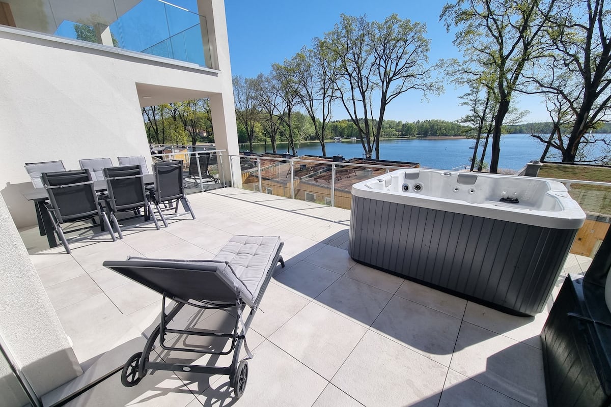 A patio with outdoor furniture, a hot tub, and a view of a lake.