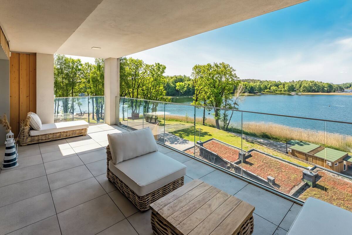 A balcony with a view of a lake, wicker furniture, and a wooden table.