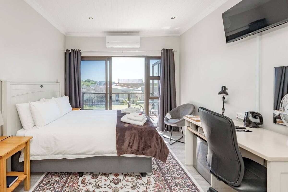 A modern hotel room with a bed, desk, chair, and a large window with curtains.