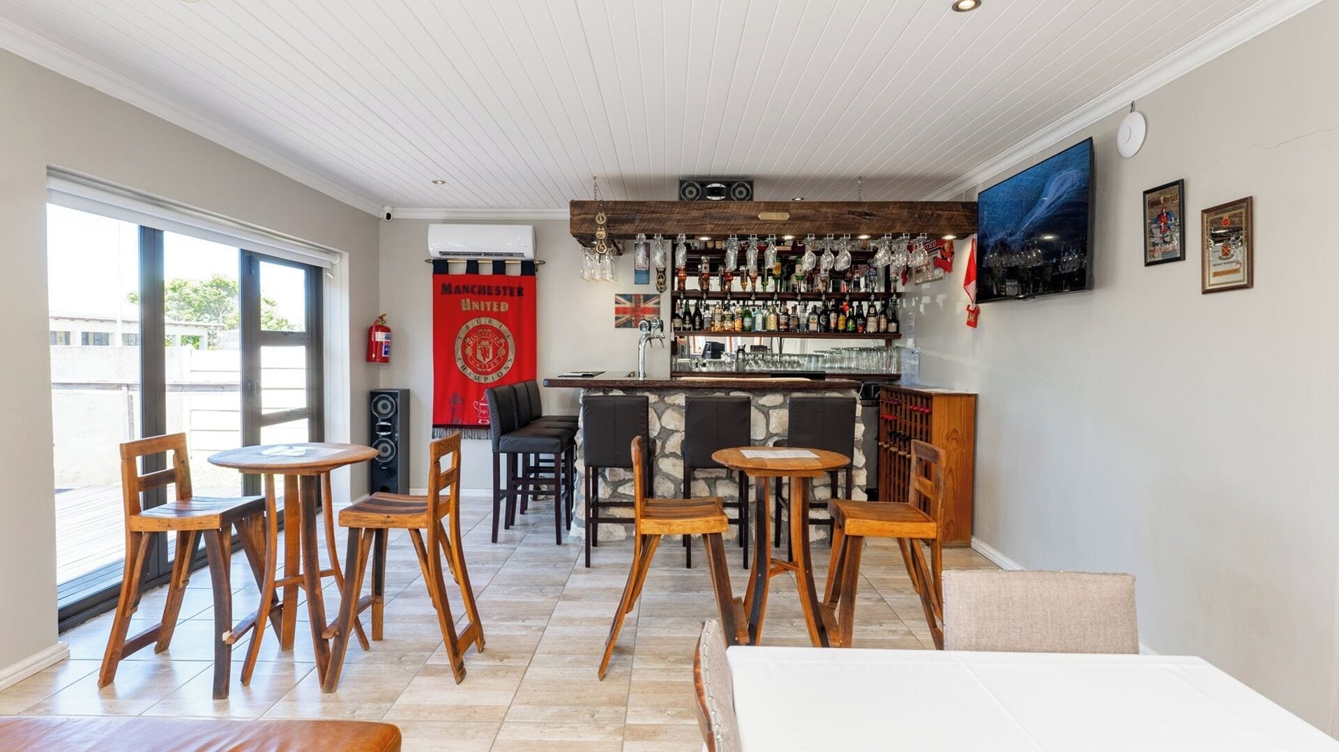 A bar area with wooden chairs, a stone wall, a Manchester United banner, and a variety of bottles.