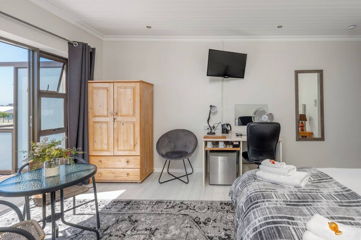 A hotel room with a bed, a desk, a chair, a wardrobe, a TV, and a window with curtains.