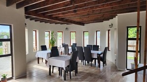 Un comedor con mesas y sillas, ventanas amplias y techo de madera.