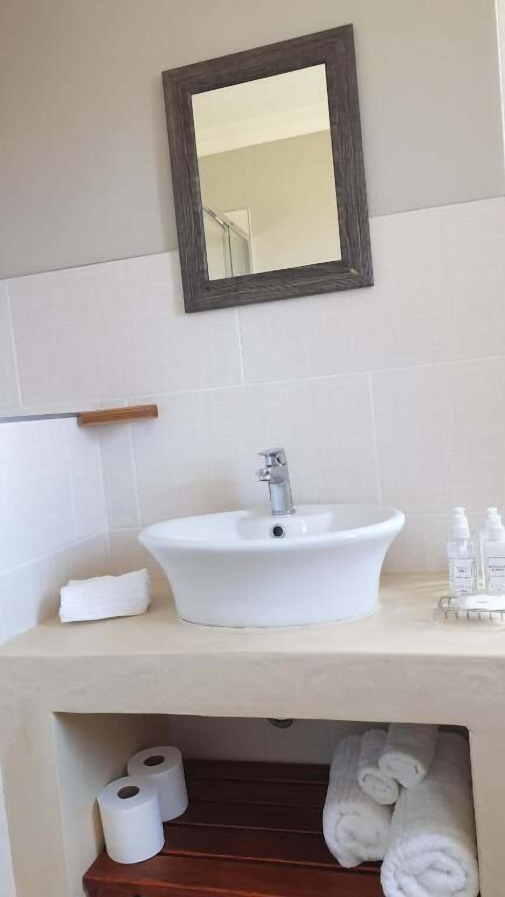 A bathroom with a white sink, a mirror, a towel rack, and a shelf with toiletries.
