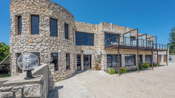 Un bâtiment en pierre doté d’une façade incurvée, de grandes fenêtres et d’un balcon avec des sièges pour l’extérieur.