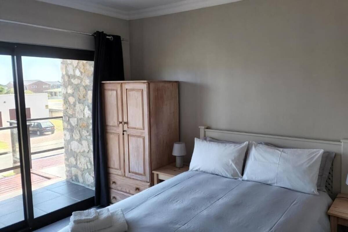 A bedroom with a bed, two bedside tables with lamps, a wardrobe, and a view through a glass door.