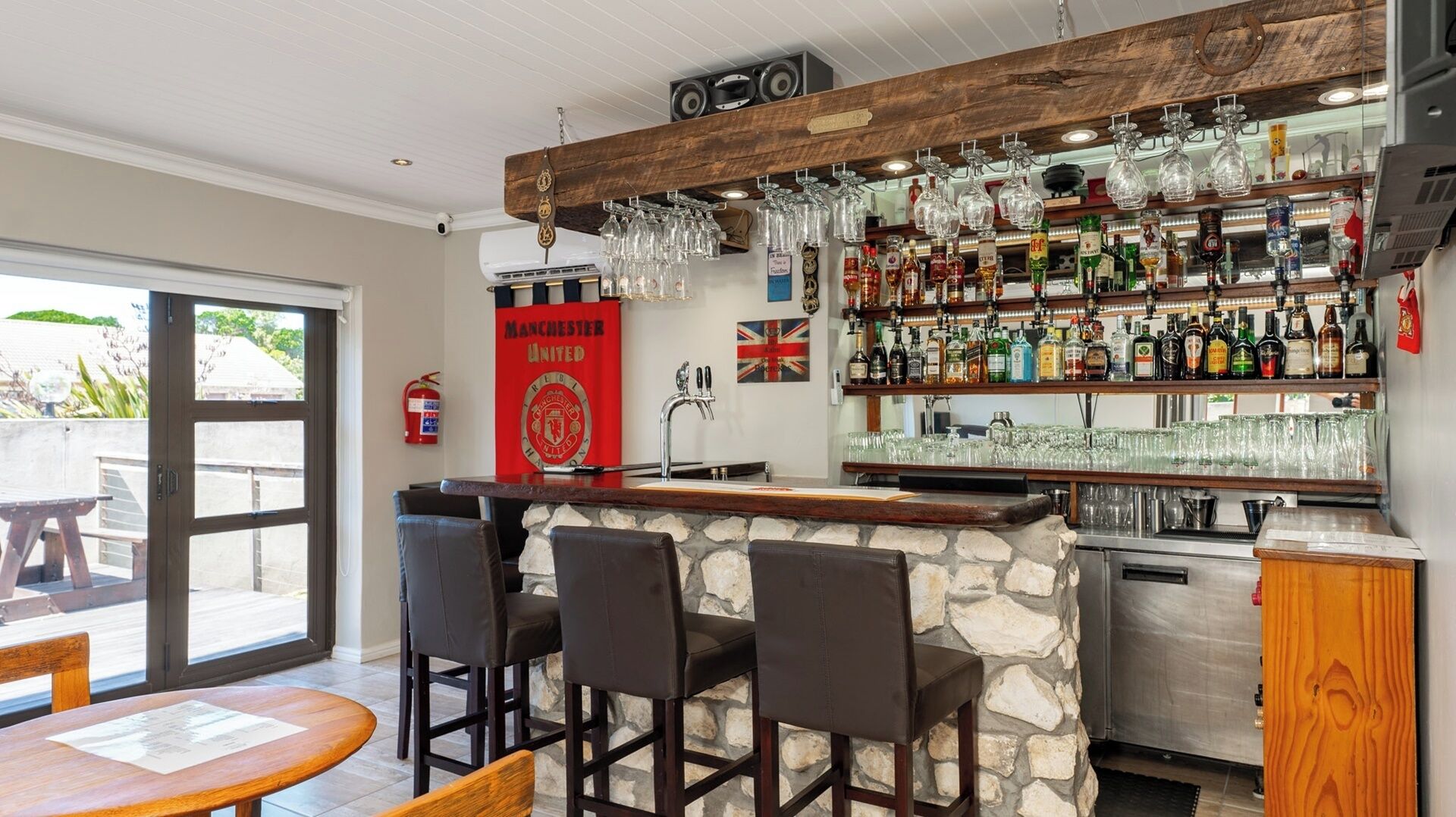 A bar area with a stone counter, multiple bar stools, a variety of bottles, and a flag on the wall.