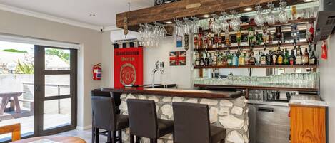 A bar area with a stone counter, multiple bar stools, a variety of bottles, and a flag on the wall.