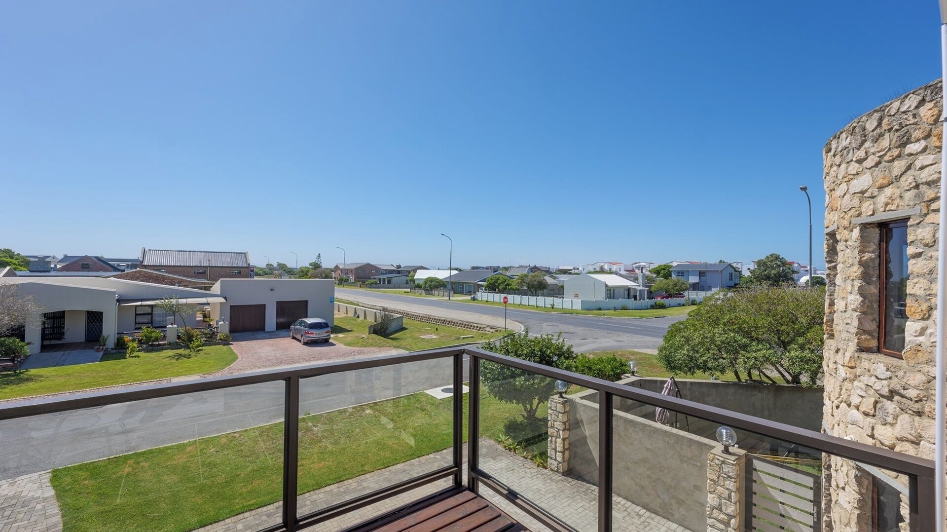 A residential area with houses, a clear sky, and a balcony with a stone wall.