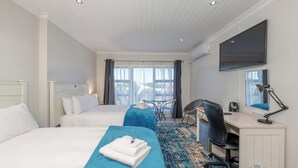 Une chambre d’hôtel avec deux lits, un bureau, une chaise, une télévision et une grande fenêtre avec des rideaux.