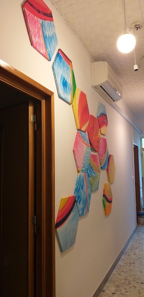 Un pasillo con arte abstracto de colores en la pared, una puerta de madera y un equipo de aire acondicionado.