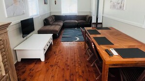 Ein Wohnzimmer mit Ecksofa, Fernseher, Esstisch mit Stühlen und Kamin.