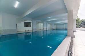 Une piscine intérieure à l’eau d’un bleu cristallin, aux murs recouverts de carreaux et dotée d’une architecture moderne.