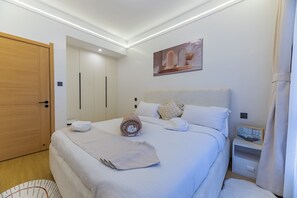 A neatly made bed with a rolled towel, a bedside table with a picture frame, and a wooden wardrobe. - Pendo Nest Suites - Cozy City Escape in Kilimani|Fast Wi-Fi| heated pool|Gym (Nairobi)