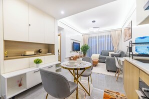 Un soggiorno moderno con zona pranzo, divano, televisore e un'ampia finestra con tende.