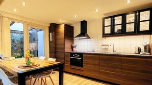 A modern kitchen with wooden cabinets, a built-in oven, and a dining area with a table and chairs. - Real Zeeland tranquility within walking distance of the Oosterschelde estuary (Stavenisse)