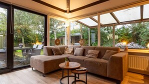 A modern living room with a sectional sofa, a round coffee table, and large windows offering a view of the outdoors. - Real Zeeland tranquility within walking distance of the Oosterschelde estuary (Stavenisse)