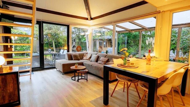 A modern living room with a wooden floor, a sofa, a dining table, and large windows. - Real Zeeland tranquility within walking distance of the Oosterschelde estuary (Stavenisse)
