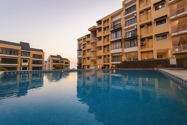 A multi-story residential building with a swimming pool in the foreground.