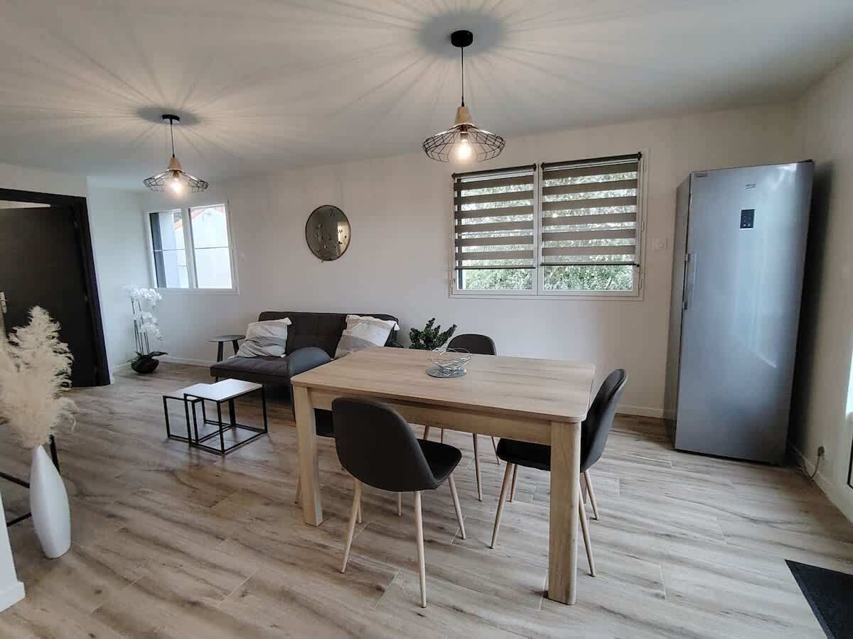 A modern kitchen with a dining table, chairs, a refrigerator, and a window with blinds.