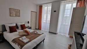 Une chambre d’hôtel avec un lit, une table de chevet, une lampe, une porte et une fenêtre avec des rideaux.