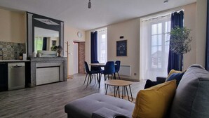 Un salon moderne comprenant un canapé, une table à manger avec des chaises, un coin cuisine avec un évier et une cuisinière, ainsi que de grandes fenêtres avec des rideaux.