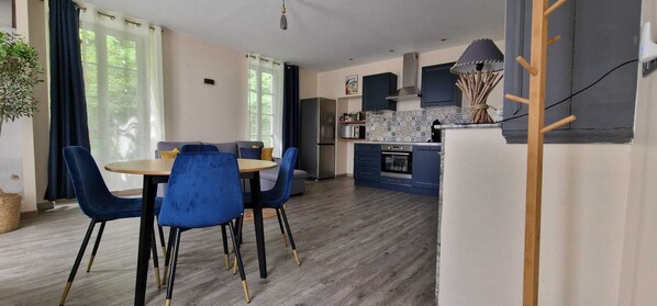 A modern kitchen with blue cabinets, a microwave, and a stove. There is a dining area with a round table and blue chairs.
