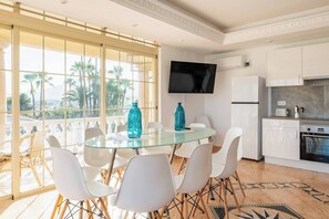 A modern kitchen with white cabinets, a TV, and a dining area with a glass table and white chairs. - Villa in Calpe near the beach (Calpe)