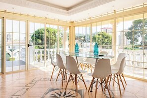 A spacious room with a glass table surrounded by chairs, large windows with a view of buildings and trees, and a patterned floor. - Villa in Calpe near the beach (Calpe)