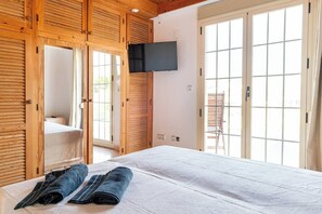 Ein Schlafzimmer mit einem Bett, einem an der Wand montierten Fernseher und einer Glastür, die zu einem Außenbereich führt.