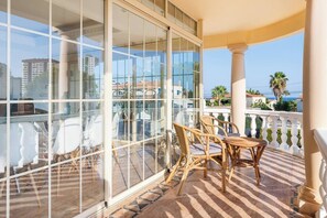 Ein Balkon mit Glastür, Korbmöbeln und Blick auf Gebäude und Palmen.