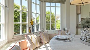 A dining area with a table set for two, large windows, and a view of greenery outside.