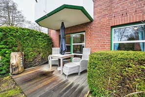 Eine Terrasse mit Tisch und Stühlen, eine Holzterrasse und ein Backsteinhaus mit grünem Fensterrahmen.