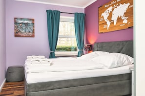 Ein Schlafzimmer mit einem Bett, einem Fenster mit Vorhängen, einer Weltkarte an der Wand und einem Gemälde.