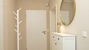 Una habitación con perchero, una puerta blanca, un aparador con cajones y un espejo redondo en la pared.