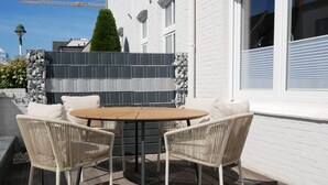 Un patio con una mesa redonda y cuatro sillas de mimbre, una pared de ladrillo blanco y una cerca de baldosas.