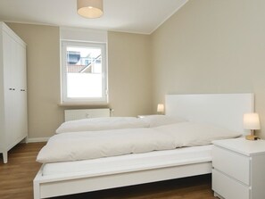 A bedroom with a bed, bedside tables, a window, and a radiator. - Jann-Berghaus-Straße 20, apartment 1 (Norderney)
