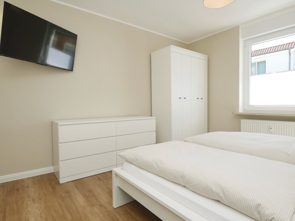 Une chambre à coucher avec un lit, une armoire, une télévision et une fenêtre.