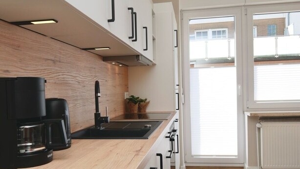 Una cocina moderna con encimera de madera, cafetera negra y ventana con vistas a edificios.