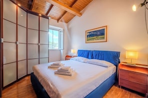 A bedroom with a bed, a nightstand, a lamp, a window, and a painting on the wall. - The Landscape Home (Roma)