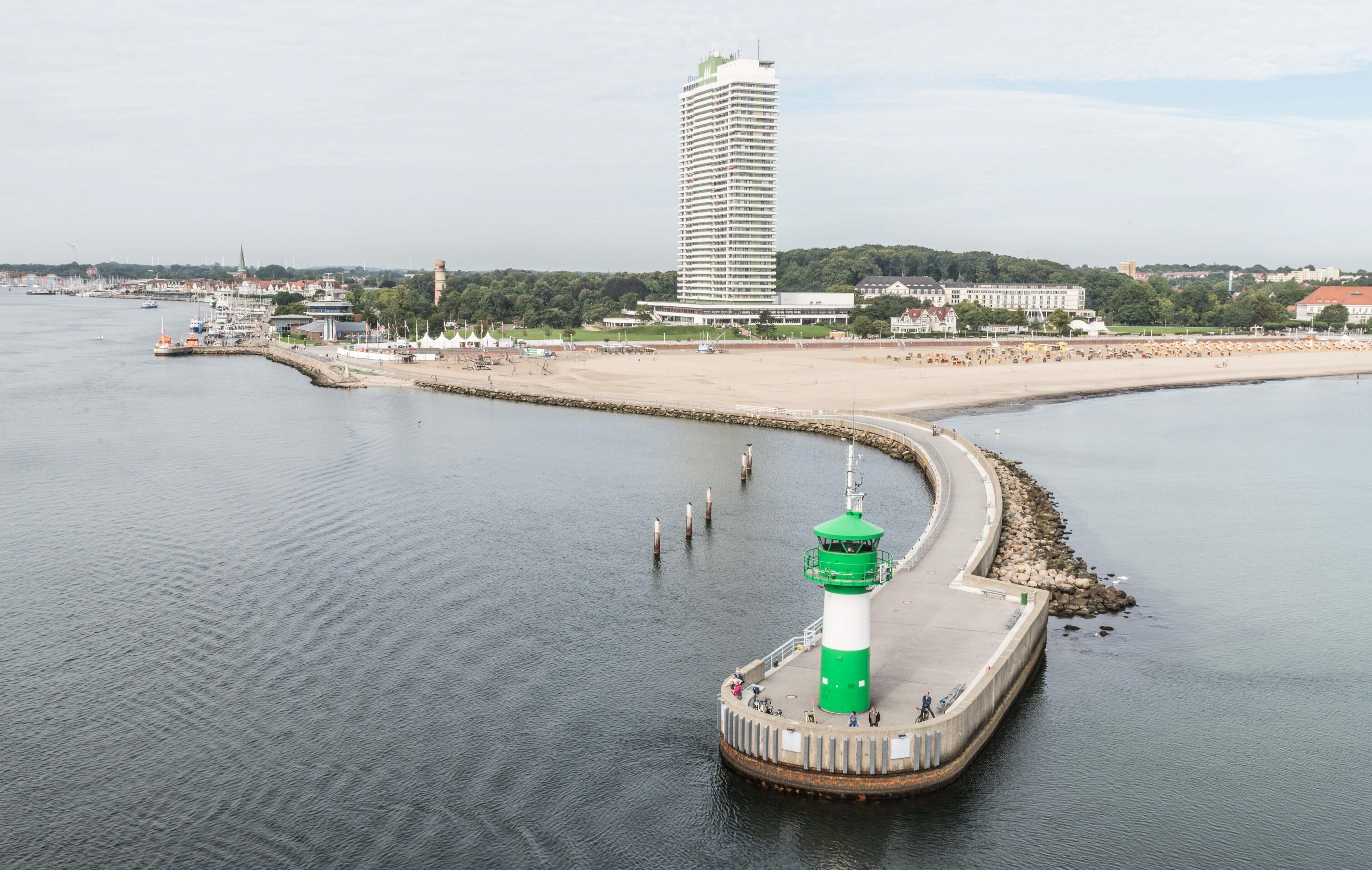 A coastal scene with a lighthouse, a beach, and a tall building in the background.