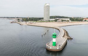 A coastal scene with a lighthouse, a beach, and a tall building in the background. - Brand-New Luxury Apartment with Baltic Sea Views in Travemünde (Lübeck)