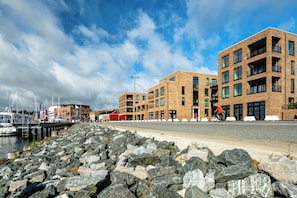 A waterfront property with a rocky shoreline, modern brick buildings, and a marina with boats. - Brand-New Luxury Apartment with Baltic Sea Views in Travemünde (Lübeck)