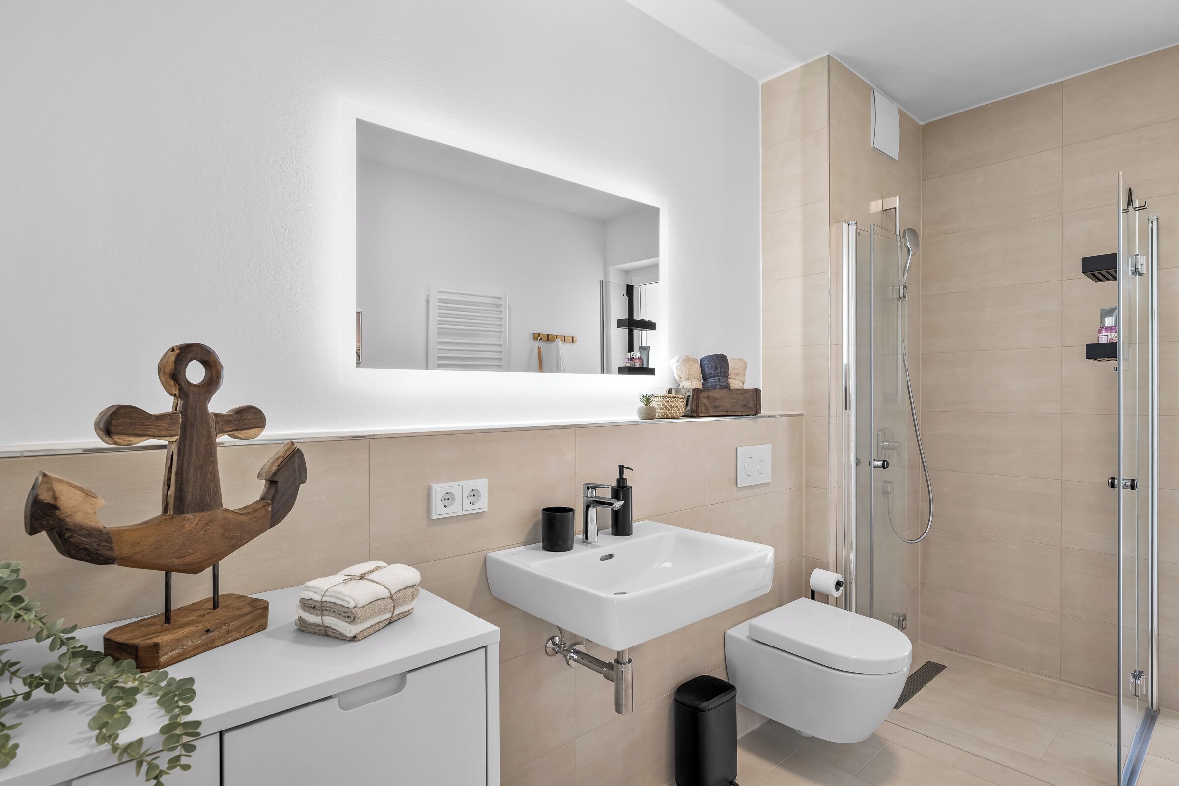A modern bathroom with a white sink, a toilet, a glass shower enclosure, and a wooden decorative piece on the vanity.