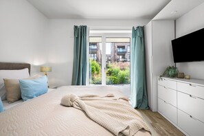 Ein Schlafzimmer mit Bett, Vorhängen, einem Fernseher und Blick auf Gebäude.
