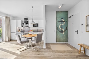 A modern kitchen with white cabinets, a dining area with grey chairs, and a large window. - Brand-New Luxury Apartment with Baltic Sea Views in Travemünde (Lübeck)