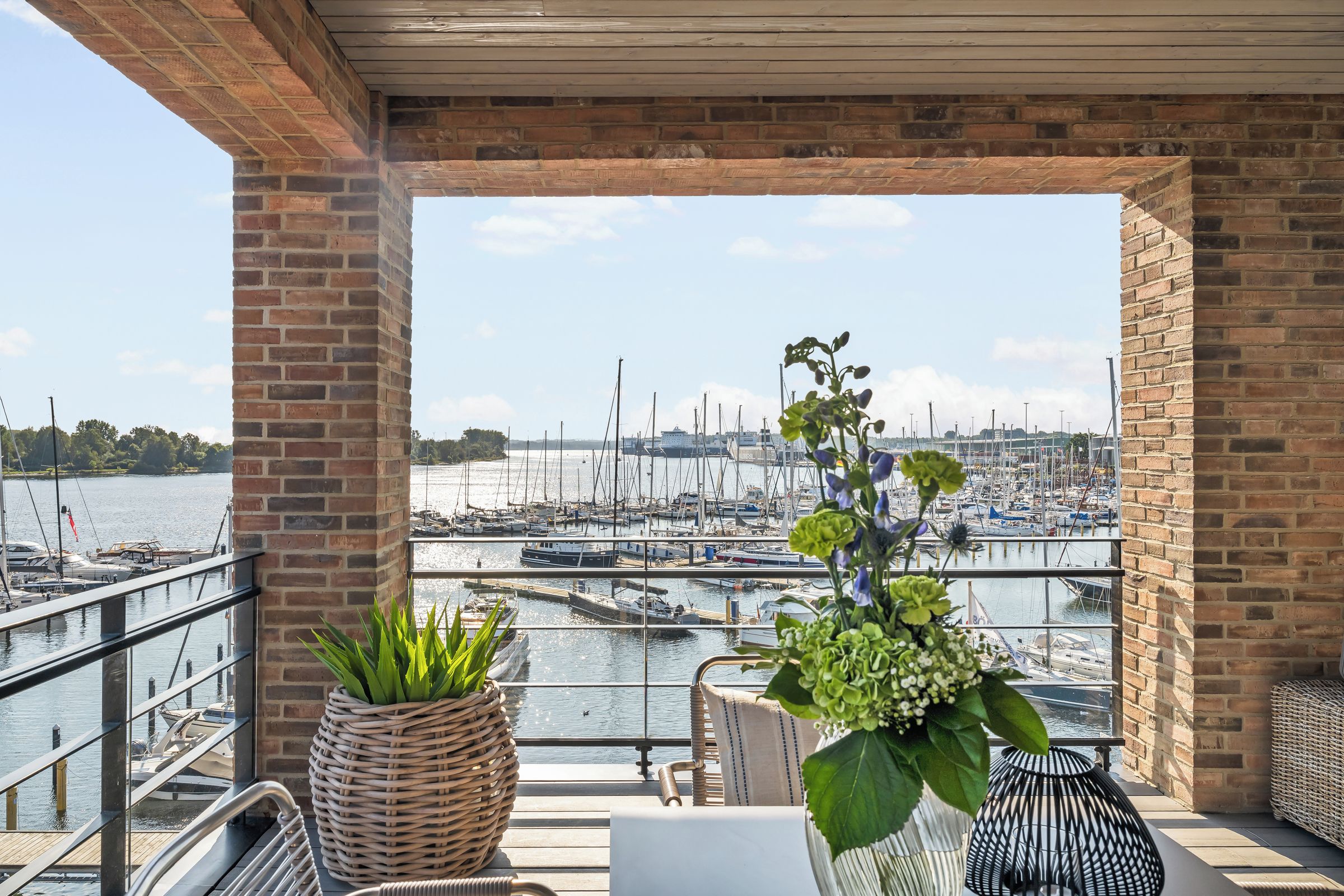 Un balcon donnant sur une marina, avec des meubles en osier et des plantes en pot.