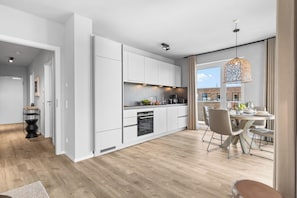 A modern kitchen with white cabinetry, a built-in oven, and a dining area with a table and chairs. - Modern Apartment Pure Travemünde with Terrace, Parking and Partial Sea View (Lübeck)