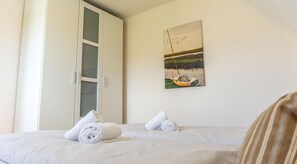 Ein Schlafzimmer mit einem Bett, zwei aufgerollten Handtüchern, einem Kleiderschrank und einem Bild von einem Boot auf dem Wasser.