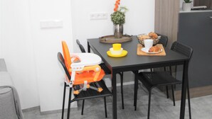Ein Essbereich mit einem Tisch, Stühlen, einem kleinen orangefarbenen Sessel, einer Topfpflanze und einer Mikrowelle über dem Tisch.