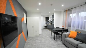 Ett modernt kök med vita skåp, ett matbord och en soffa med orange kuddar.